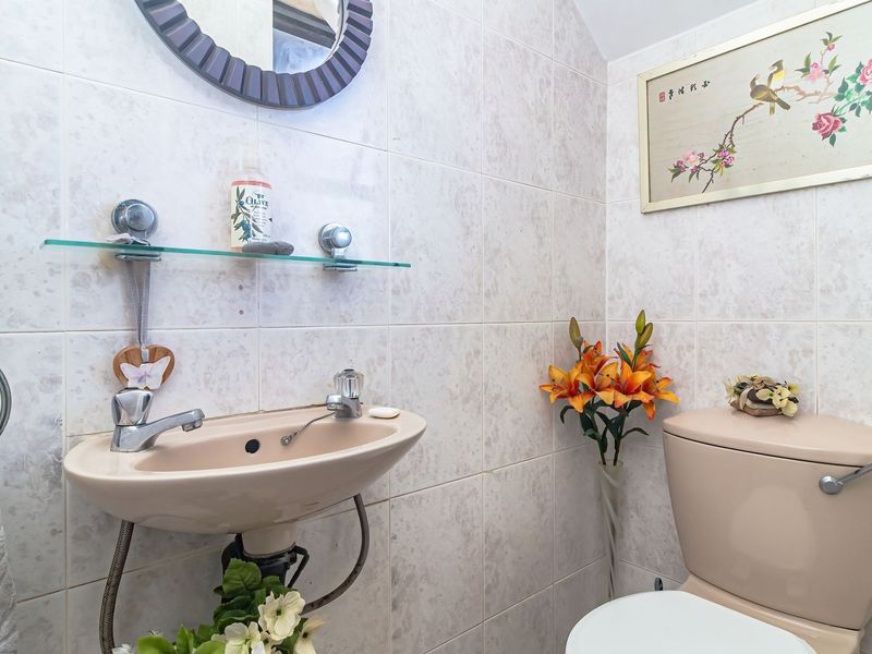 A compact bathroom featuring a wall-mounted basin, toilet, and neutral wall tiling, offering a functional space with potential for modern updates.