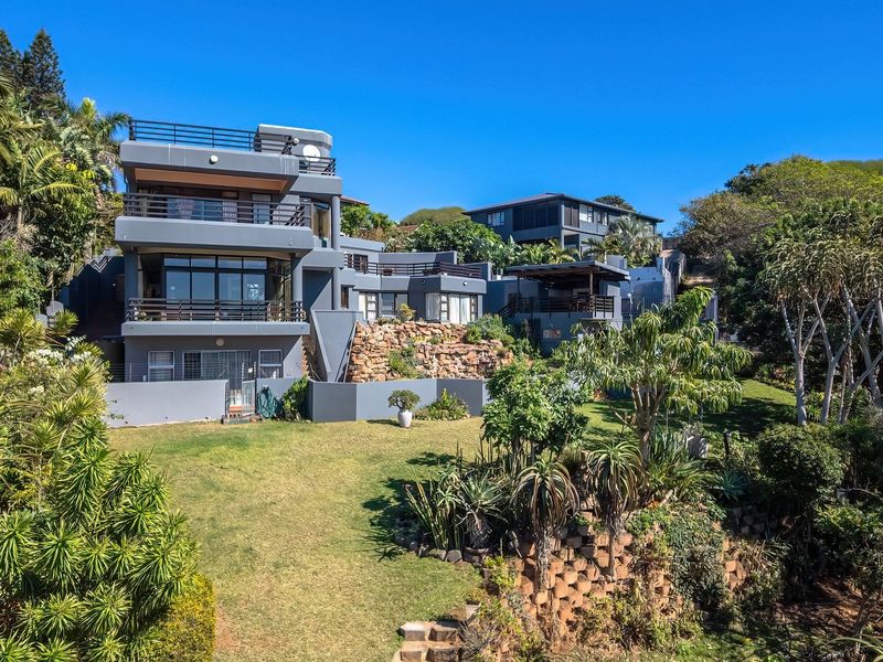 A multi-level modern residence featuring expansive balconies, stone retaining walls, and a well-maintained garden, showcasing contemporary architectural design and outdoor living spaces.