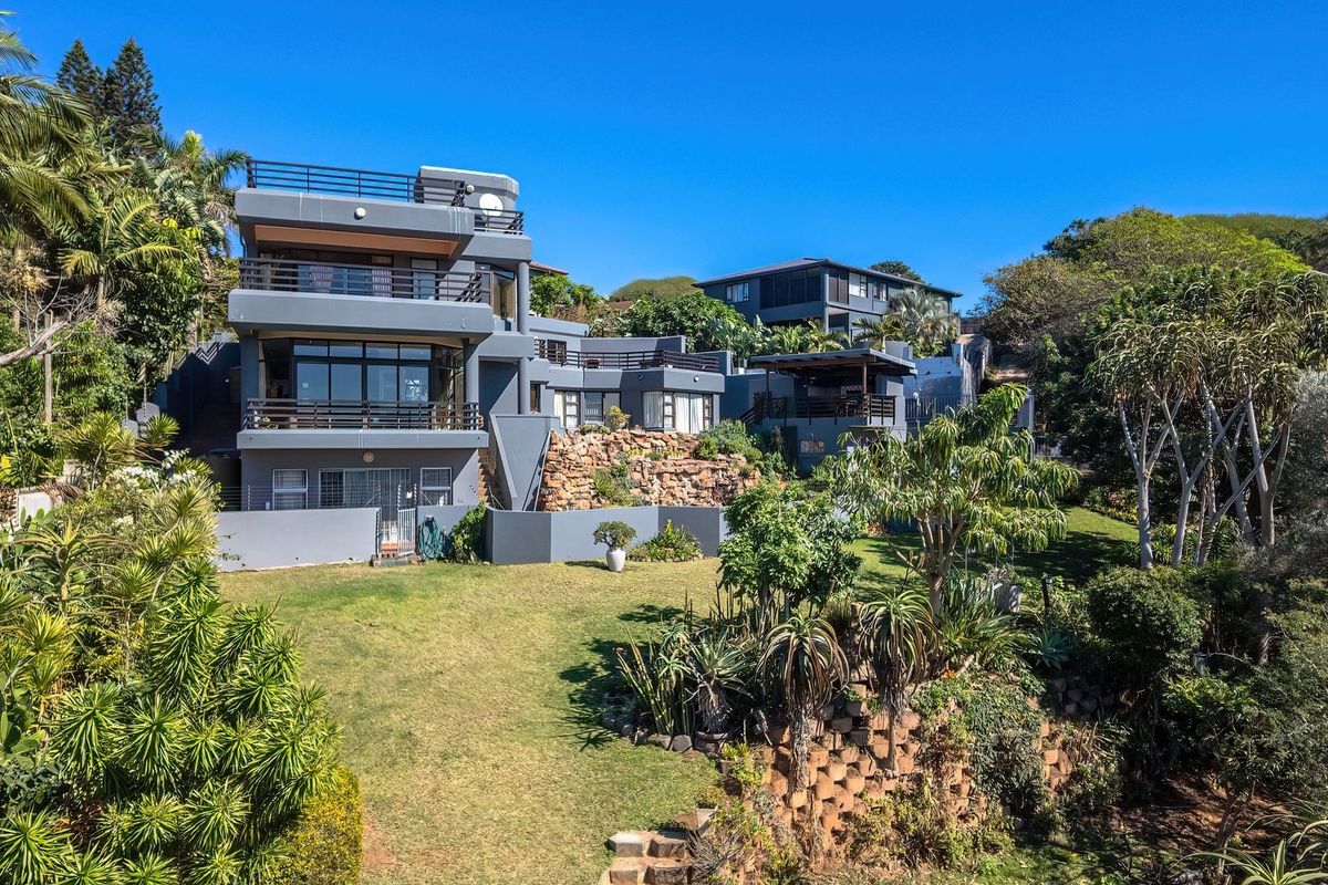 A multi-level modern residence featuring expansive balconies, stone retaining walls, and a well-maintained garden, showcasing contemporary architectural design and outdoor living spaces.