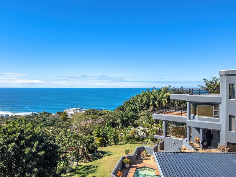 Elevated view of a multi-level coastal residence featuring a swimming pool, landscaped gardens, and expansive ocean vistas.