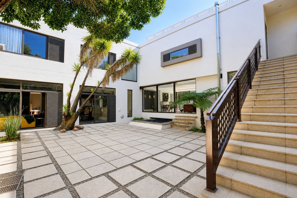 A modern, paved rear courtyard featuring an external staircase with metal balustrades, large sliding glass doors, and a built-in water feature.