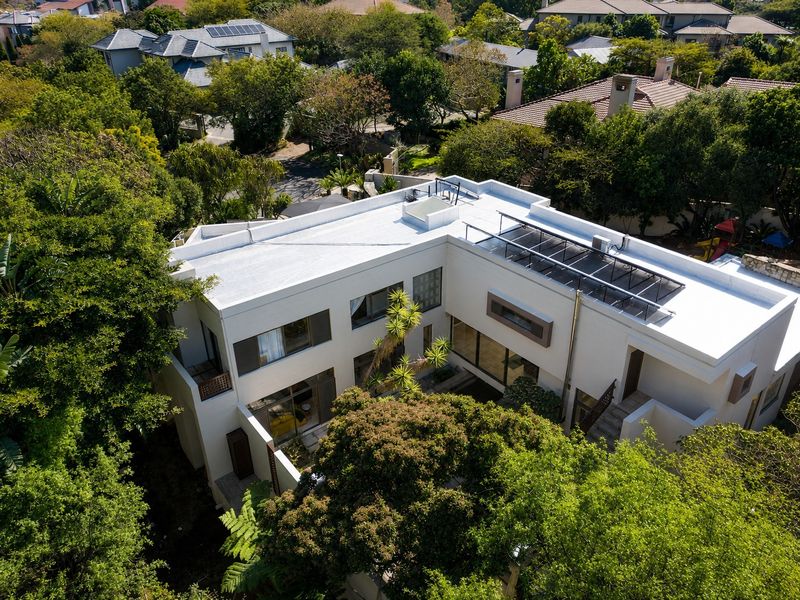 Aerial view of a modern residential property featuring a flat roof with solar panels, a central courtyard, and lush surrounding greenery.
