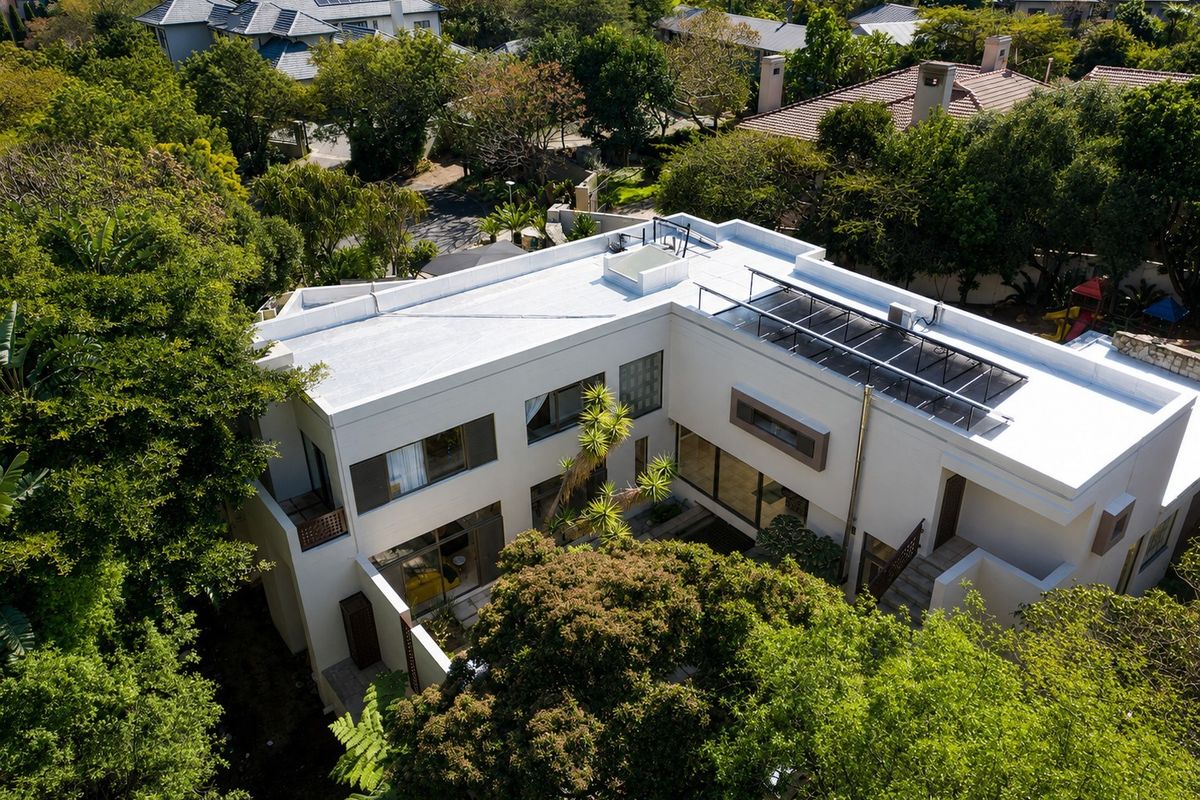 Aerial view of a modern residential property featuring a flat roof with solar panels, a central courtyard, and lush surrounding greenery.