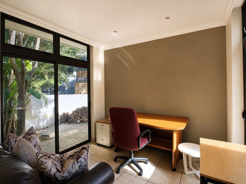 A bright home office featuring tiled flooring, recessed downlights, and large sliding glass doors providing natural light and garden access.