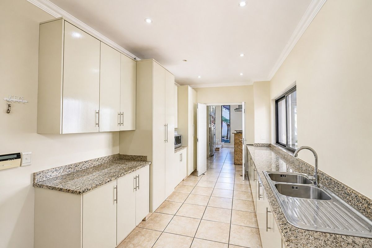 A clean, functional kitchen featuring granite countertops, ample built-in cabinetry, a double basin stainless steel sink, and tiled flooring with recessed lighting.