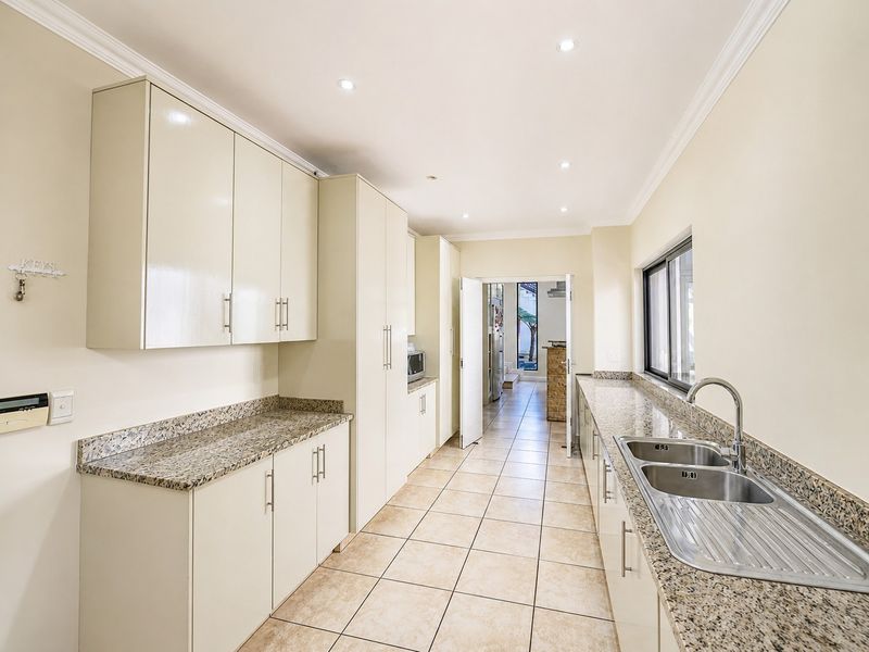 A clean, functional kitchen featuring granite countertops, ample built-in cabinetry, a double basin stainless steel sink, and tiled flooring with recessed lighting.