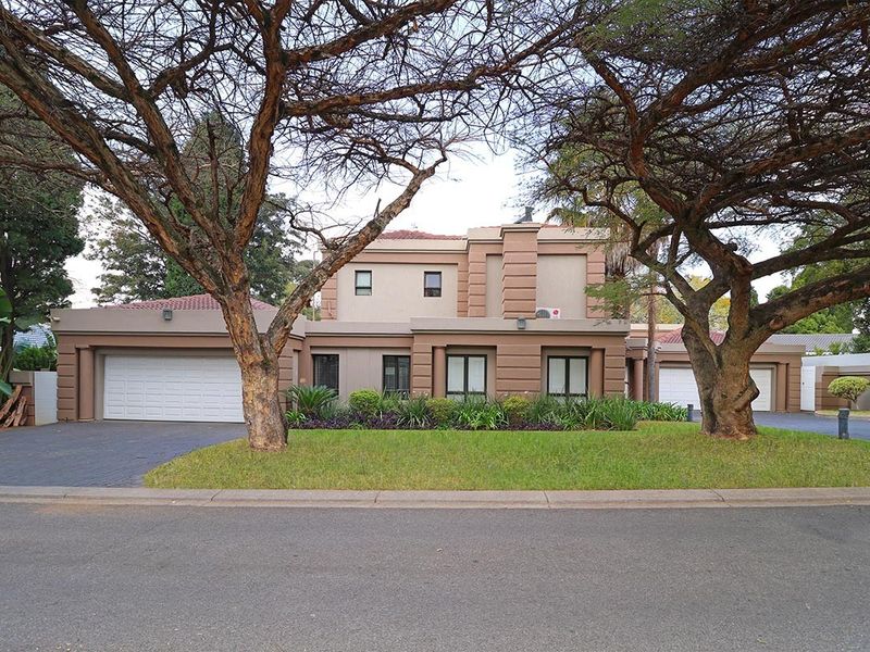 A well-maintained double-story residential property featuring a paved driveway, double garage, and established garden with mature trees.