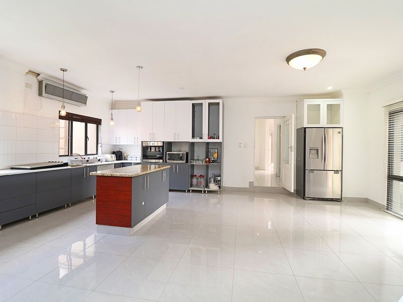 Spacious kitchen featuring a central island, granite countertops, fitted cabinetry, and built-in appliances, with tiled flooring throughout.