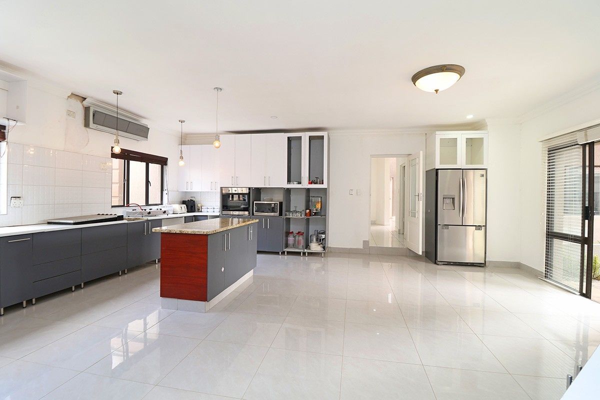 Spacious kitchen featuring a central island, granite countertops, fitted cabinetry, and built-in appliances, with tiled flooring throughout.