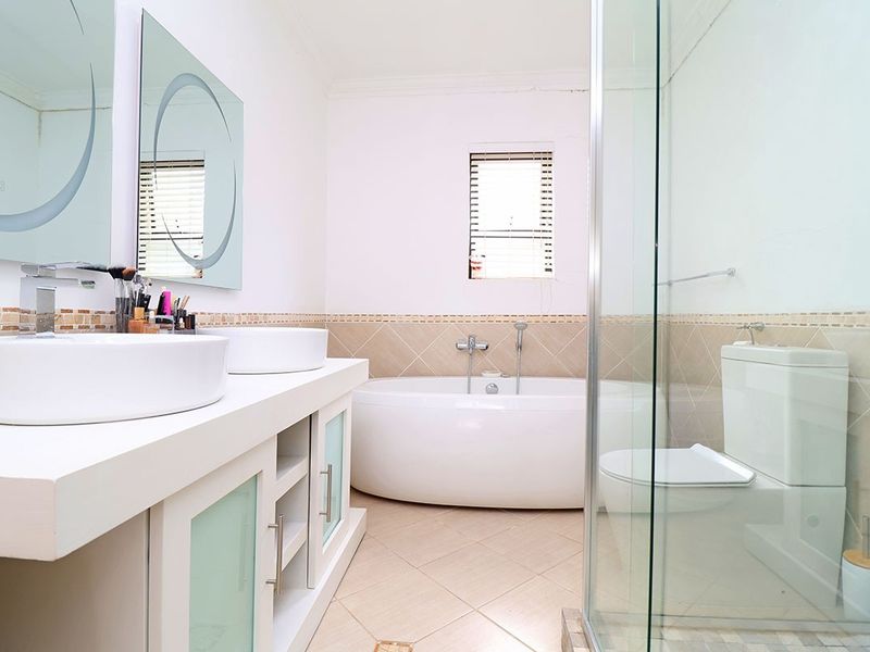 Modern bathroom featuring a double vanity with vessel sinks, a freestanding bathtub, and a separate glass-enclosed shower with neutral tiled finishes.