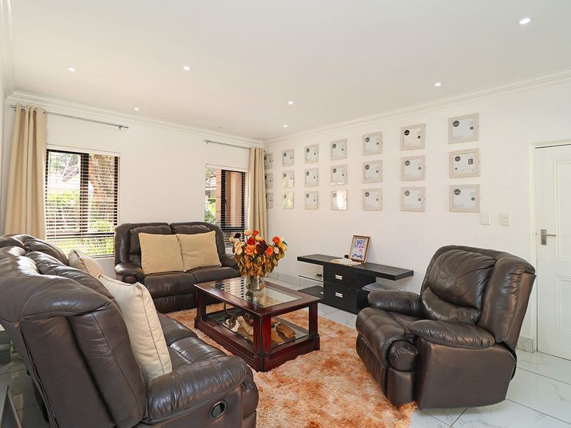 A bright and well-maintained living room featuring tiled flooring, recessed downlights, and large windows with venetian blinds.