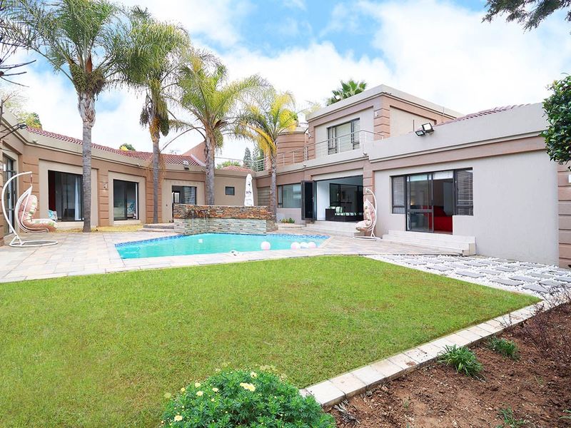 A spacious rear courtyard featuring a swimming pool with a stone water feature, paved patio area, and well-maintained lawn surrounded by the home's exterior.
