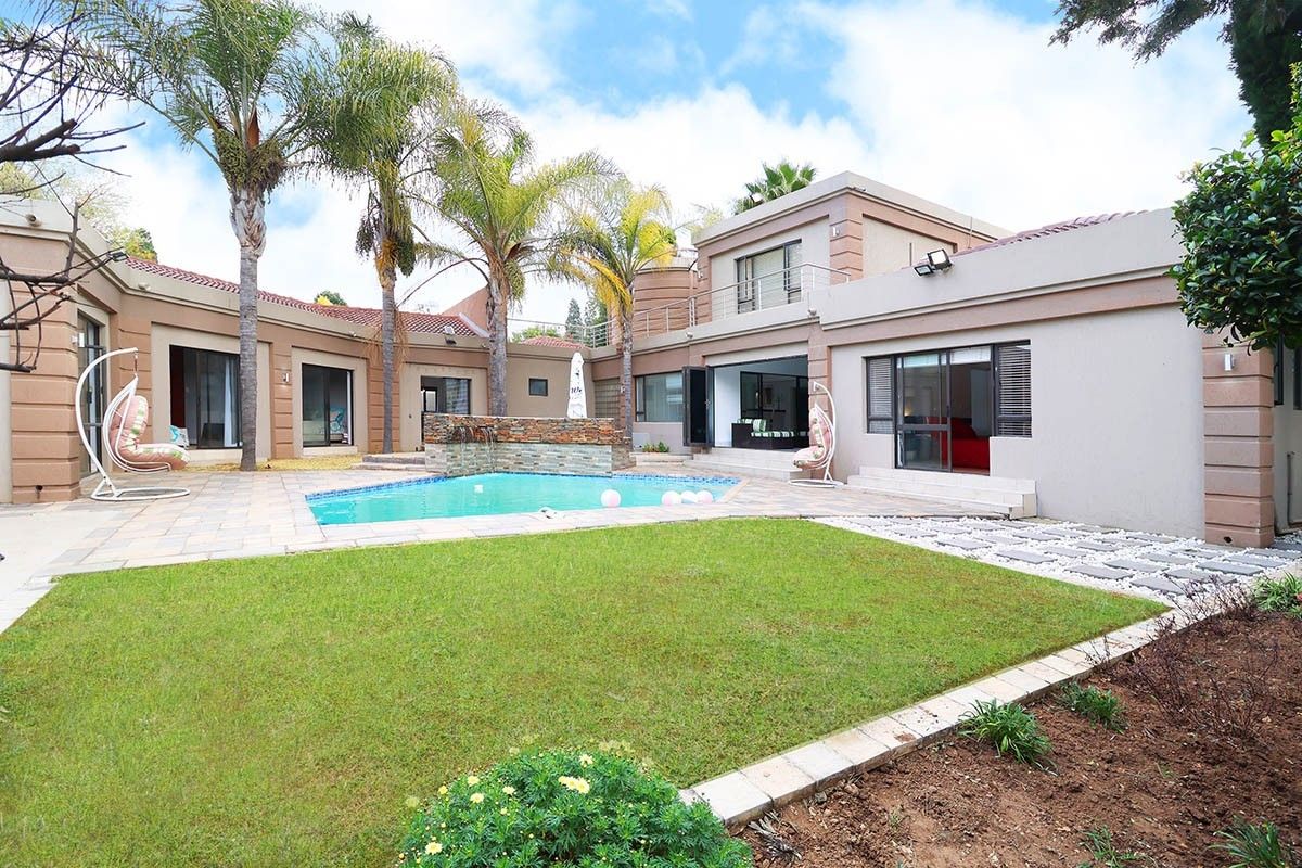 A spacious rear courtyard featuring a swimming pool with a stone water feature, paved patio area, and well-maintained lawn surrounded by the home's exterior.