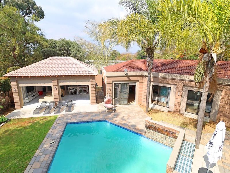 Aerial view of a rear garden featuring a swimming pool, water feature, paved patio, and a covered outdoor entertainment area.