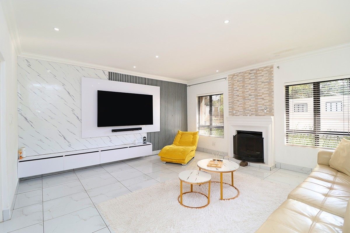 Modern living room featuring a built-in media console, marble-effect wall cladding, a fireplace with stone detailing, and tiled flooring throughout.
