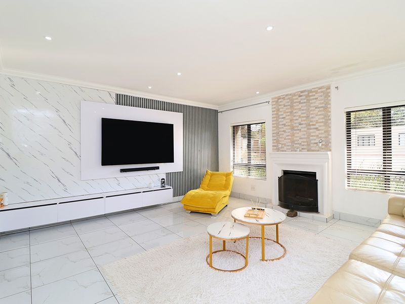 Modern living room featuring a built-in media console, marble-effect wall cladding, a fireplace with stone detailing, and tiled flooring throughout.