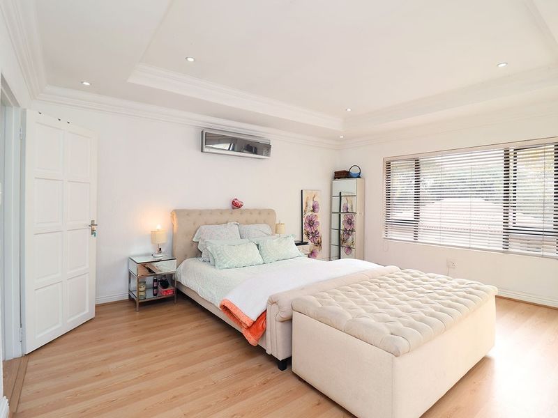 A well-maintained bedroom featuring laminate flooring, a recessed ceiling with downlights, and a wall-mounted split-system air conditioner.