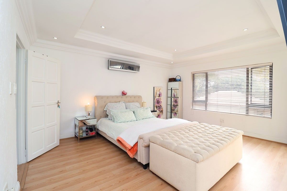 A well-maintained bedroom featuring laminate flooring, a recessed ceiling with downlights, and a wall-mounted split-system air conditioner.