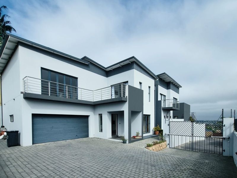 Modern double-story residential property featuring a paved driveway, integrated double garage, and upper-level balcony with contemporary architectural finishes.