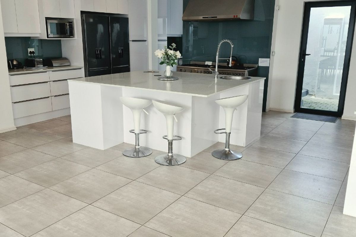 Modern kitchen featuring a central island with quartz countertops, sleek white cabinetry, integrated appliances, and large format floor tiles.