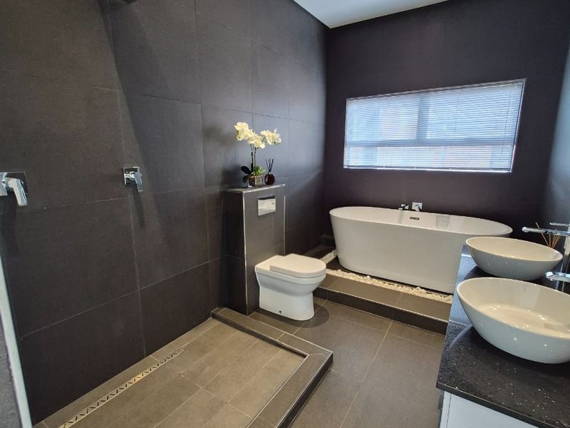 Modern bathroom featuring a walk-in shower, freestanding bathtub, double vanity with vessel sinks, and dark contemporary tiling.