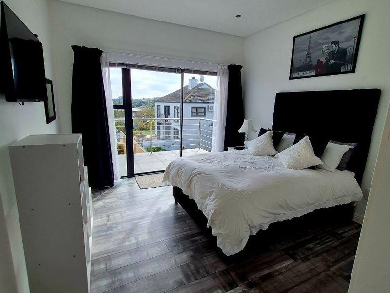 A modern bedroom featuring laminate flooring, recessed lighting, and a large sliding glass door providing access to an outdoor balcony.