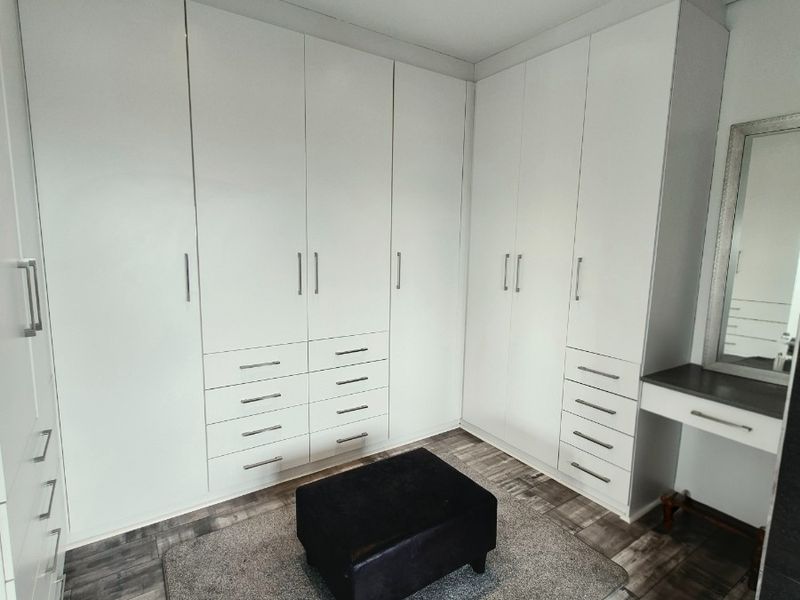 A modern bedroom featuring extensive white built-in cabinetry with integrated drawers and a dedicated vanity area, finished with contemporary wood-look flooring.