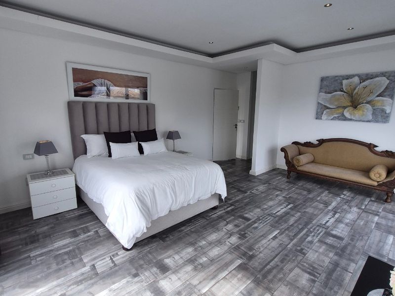 Spacious bedroom featuring modern grey-toned laminate flooring, recessed tray ceiling lighting, and a neutral color palette.