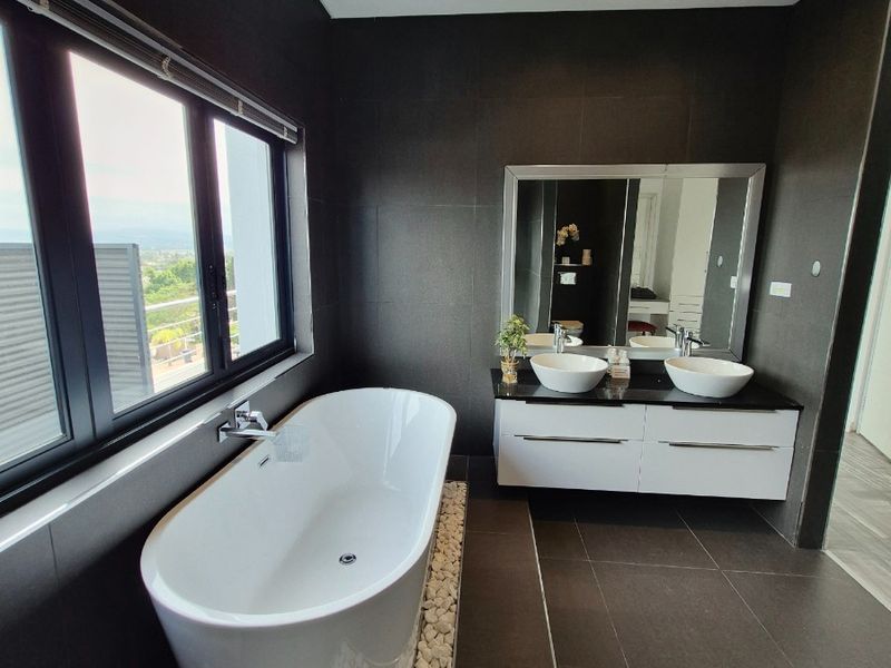 Modern bathroom featuring a sleek freestanding bathtub, double vanity with vessel sinks, and dark tiled finishes with recessed lighting.