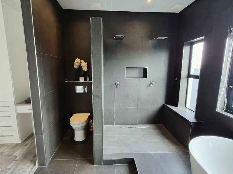 Modern luxury bathroom featuring a spacious walk-in shower with dual shower heads, a sleek wall-mounted toilet, and a contemporary freestanding bathtub.