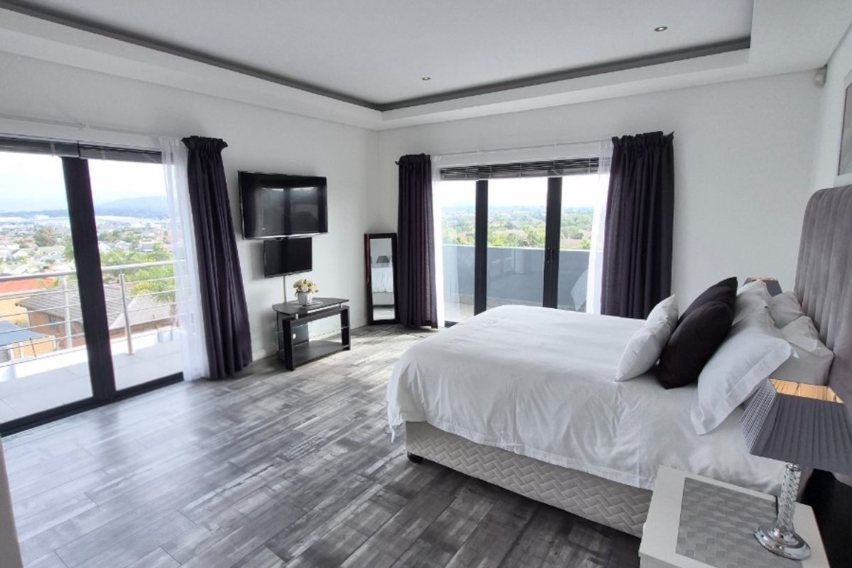 Spacious bedroom featuring modern wood-look tile flooring, recessed tray ceiling lighting, and dual sliding glass doors opening onto a private balcony with scenic views.