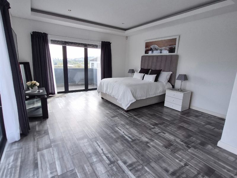 Spacious bedroom featuring modern tray ceilings, recessed lighting, wood-look laminate flooring, and direct access to a private balcony through sliding glass doors.