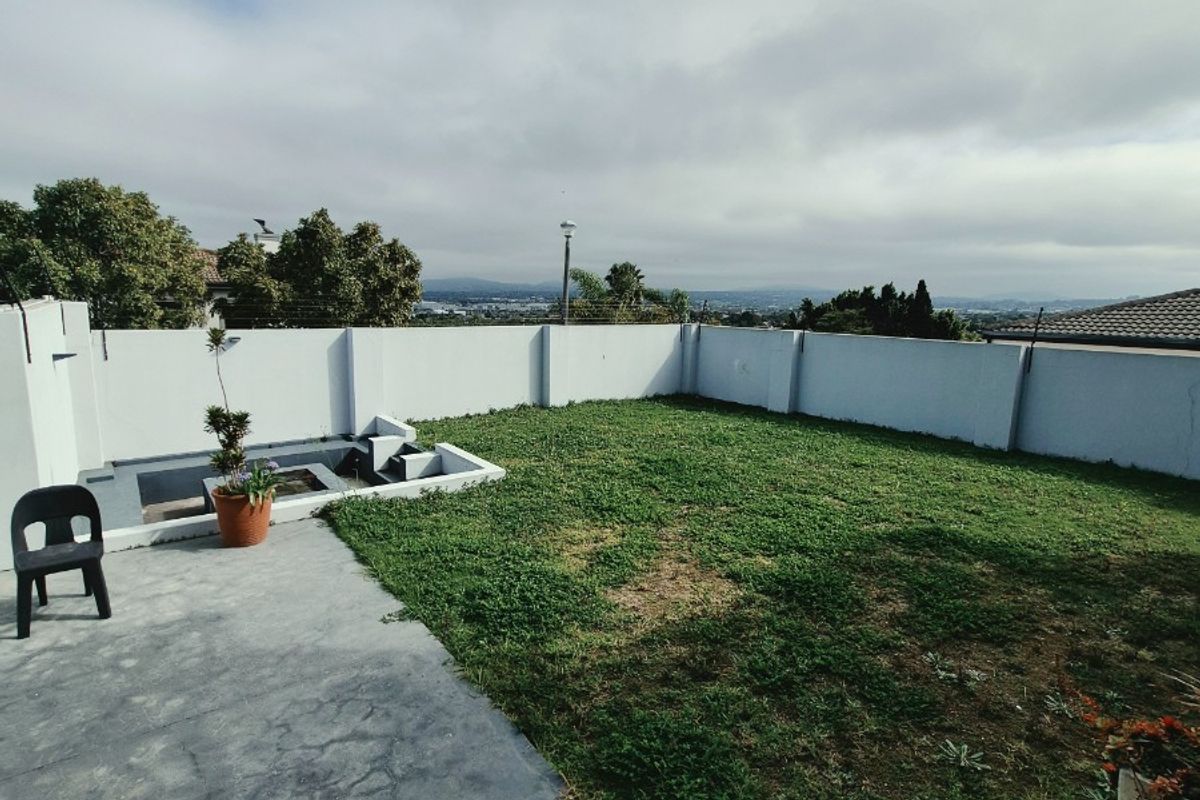 A rear garden area featuring a concrete patio, a sunken water feature, and a perimeter boundary wall with distant views.