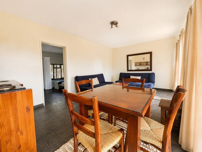 Open plan living and dining area featuring dark tiled flooring and neutral wall finishes, providing a functional space with access to an adjacent bedroom.