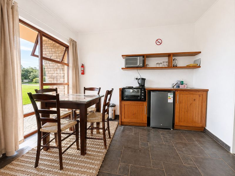 Open-plan kitchenette and dining area featuring tiled floors, wooden cabinetry, built-in shelving, and direct access to an outdoor patio through a large glass door.