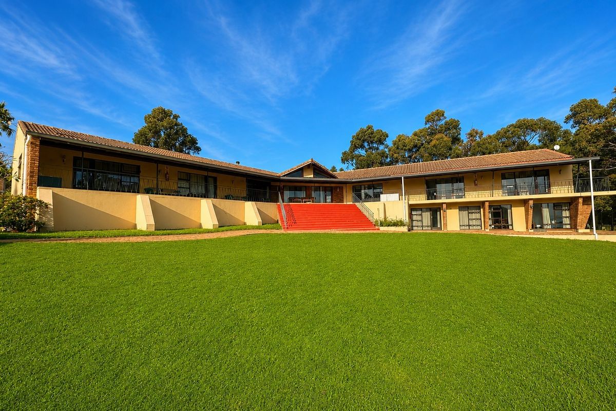 A spacious rear exterior view of the property featuring a large manicured lawn, a central staircase, and an expansive balcony overlooking the garden.