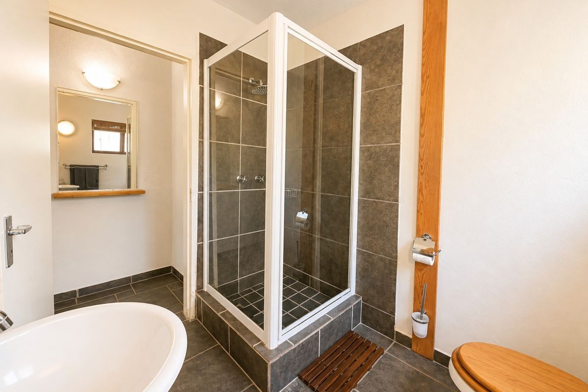 A well-maintained bathroom featuring a glass-enclosed shower, tiled finishes, a wall-mounted mirror, and a toilet with a wooden seat.