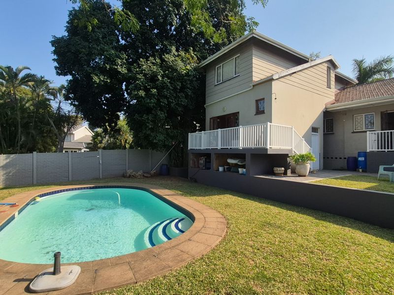 Rear exterior view featuring a swimming pool, raised deck area, and a well-maintained garden with perimeter walling.