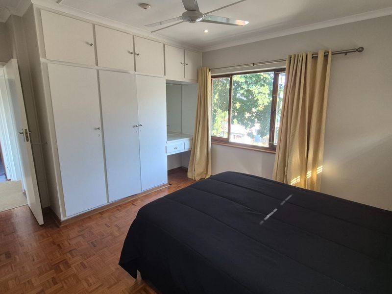 A well-maintained bedroom featuring classic parquet flooring, extensive built-in cabinetry with an integrated vanity, and a ceiling fan for climate control.