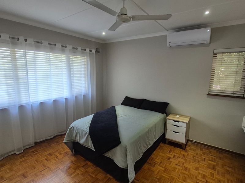 A well-maintained bedroom featuring classic parquet flooring, a ceiling fan, split-system air conditioning, and built-in storage cupboards.
