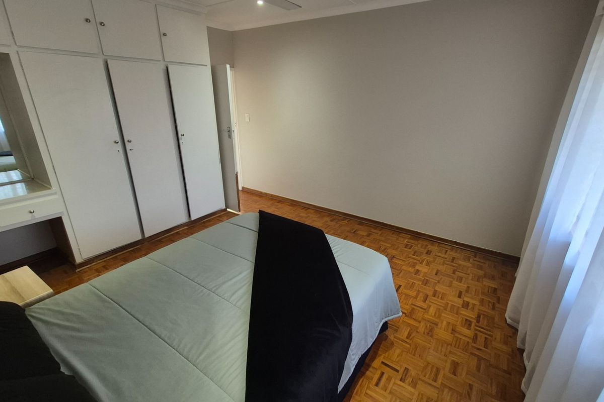 A bedroom featuring classic parquet flooring and extensive built-in cupboard storage with an integrated vanity area.