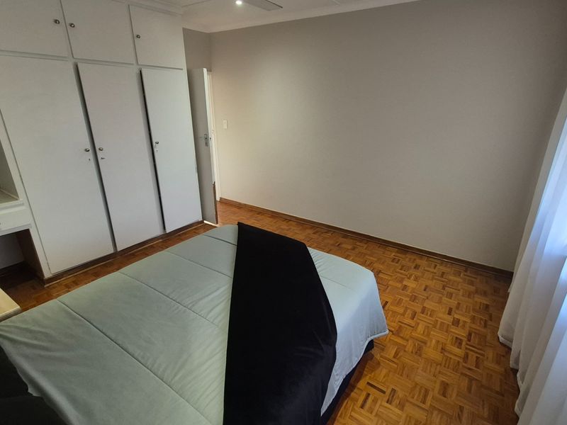 A bedroom featuring classic parquet flooring and extensive built-in cupboard storage with an integrated vanity area.