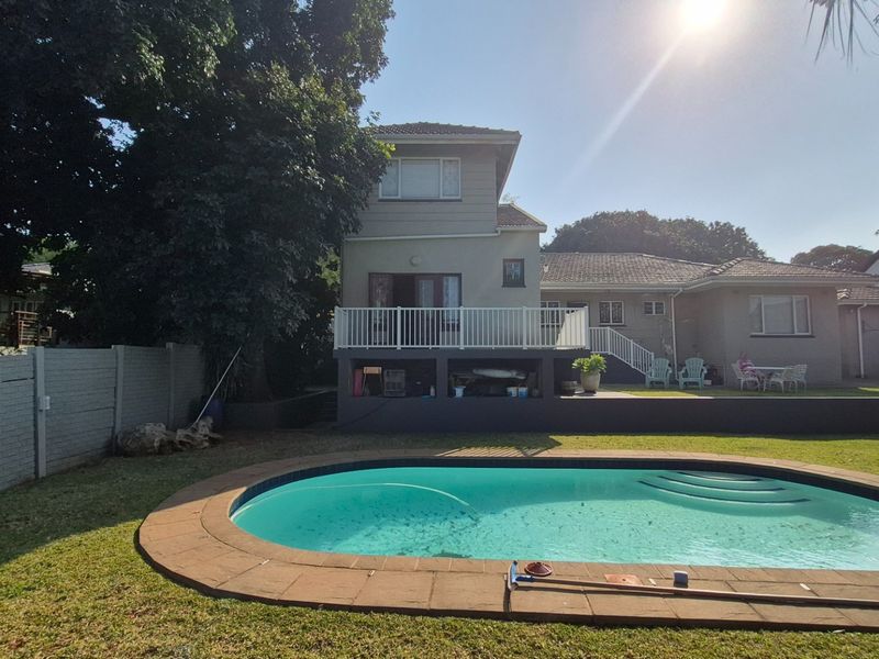 Rear view of the property featuring a swimming pool, a raised deck with white railings, and a landscaped garden area.