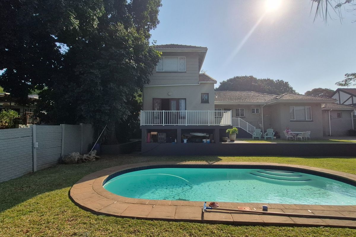 Rear view of the property featuring a swimming pool, a raised deck with white railings, and a landscaped garden area.