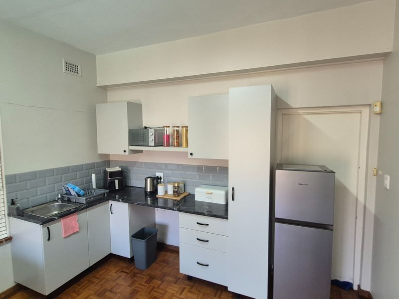 A functional kitchen featuring white cabinetry, dark laminate countertops, a subway tile backsplash, and classic parquet flooring.