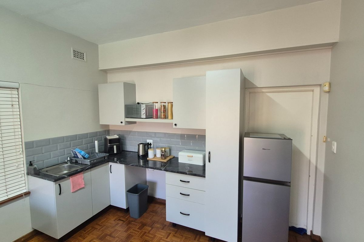 A functional kitchen featuring white cabinetry, dark laminate countertops, a subway tile backsplash, and classic parquet flooring.