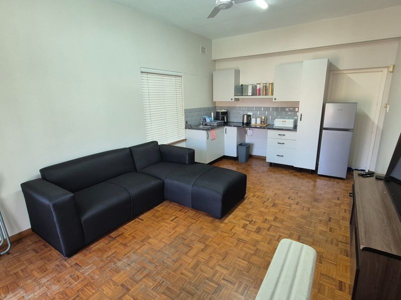 Open-plan living area featuring parquet flooring, a compact kitchen with built-in cabinetry, subway tile backsplash, and a ceiling fan.