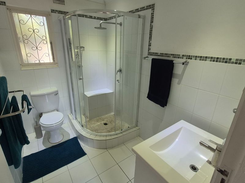 A functional bathroom featuring a corner shower enclosure with a built-in seat, a standard toilet, and a vanity basin with tiled finishes.