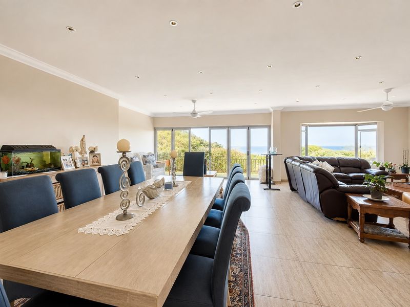 Spacious open-plan living and dining area featuring tiled floors, recessed lighting, and large sliding doors that open to scenic coastal views.