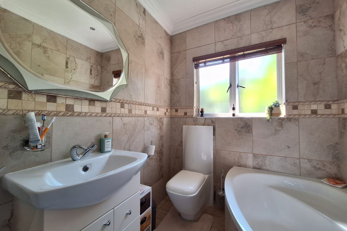 A well-maintained bathroom featuring neutral stone-look wall tiles, a modern vanity with basin, a toilet, and a bathtub under a window.